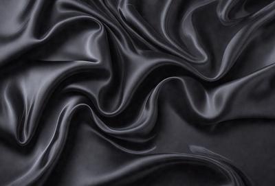 The primary subject of the image is a close-up of a black fabric, possibly a piece of clothing or a curtain. The setting is a dark background, which emphasizes the fabric's texture and pattern. The visual style appears to be a photo, as it captures the details of the fabric. The colors and mood of the image are predominantly dark, with the black fabric being the main focus.