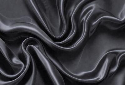 The primary subject of the image is a close-up of a black fabric, possibly a piece of clothing or a curtain. The setting is a dark room, and the visual style appears to be a photo. The colors and mood of the image are predominantly dark and moody, with the black fabric being the main focus.