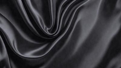 The primary subject of the image is a black fabric, which appears to be a piece of silk. The setting is a dark background, which contrasts with the fabric. The visual style is a close-up of the fabric, showcasing its texture and pattern. The colors and mood of the image are predominantly dark, with the black fabric being the main focus.
