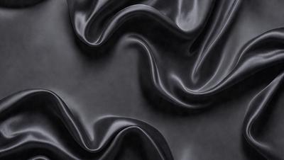 The primary subject of the image is a close-up of a black fabric, possibly leather, with a pattern of wrinkles and folds. The setting is a dark background, which emphasizes the fabric's texture and pattern. The visual style appears to be a close-up photo of the fabric, showcasing its unique texture and appearance. The colors and mood of the image are predominantly dark, with the black fabric being the main focus.