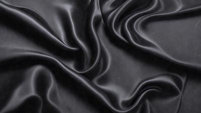 The primary subject of the image is a close-up of a black fabric, possibly a piece of leather or a similar material. The setting is a dark background, which emphasizes the fabric's texture and appearance. The visual style is a close-up, focusing on the details of the fabric. The colors and mood of the image are predominantly dark, with the black fabric being the main focus.