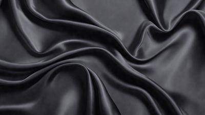 The primary subject of the image is a close-up of a black fabric, possibly a piece of leather or a curtain. The setting is a dark background, which emphasizes the fabric's texture and color. The visual style is a black and white photo, which adds a timeless and classic feel to the image. The colors and mood are predominantly dark and moody, with the black fabric serving as the focal point of the scene.