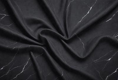 The primary subject of the image is a black fabric, possibly a piece of cloth or a curtain. The setting is a black background, which provides a stark contrast to the fabric. The visual style appears to be a close-up of the fabric, showcasing its texture and details. The colors and mood of the image are predominantly dark, with the black fabric being the main focus.