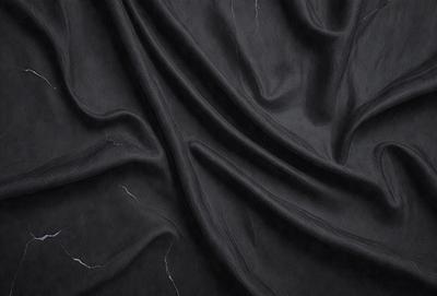 The primary subject of the image is a black fabric, possibly a curtain or a piece of clothing. The setting is a dark room, and the visual style appears to be a close-up of the fabric. The colors and mood of the image are predominantly dark and moody, with the black fabric as the main focus.