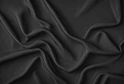 The primary subject of the image is a close-up of a black fabric, possibly a piece of clothing or a curtain. The setting is a dark background, which emphasizes the fabric's texture and pattern. The visual style is a close-up, which allows the viewer to appreciate the details of the fabric. The colors and mood of the image are predominantly dark, creating a moody and dramatic atmosphere.