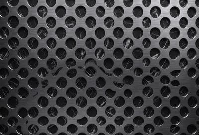 The primary subject of the image is a close-up of a metal surface with a pattern of holes. The setting is a black background, and the visual style appears to be a photo. The dominant colors are black and silver, creating a sleek and modern atmosphere.