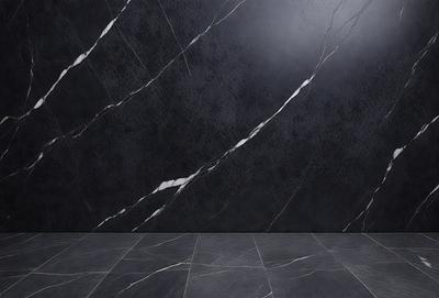 The primary subject of the image is a marble wall with a black background. The setting is a room with a black floor, and the visual style is a photo. The colors and mood of the image are dark and moody, with the marble wall and black floor creating a dramatic and sophisticated atmosphere.