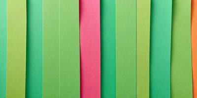 The primary subject of the image is a row of three different colored papers, which are green, pink, and red. The setting is a table, and the visual style is a close-up of the papers. The colors and mood of the image are vibrant and lively, with the green, pink, and red colors creating a cheerful atmosphere.