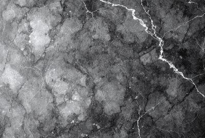 The image is a black and white photo of a marble wall. The marble wall has a pattern of holes and is textured, giving it a unique appearance. The wall is the primary subject of the image, and it is set against a black background. The visual style of the image is a photo, and the dominant colors are black and white. The overall atmosphere of the image is elegant and sophisticated, as marble is often associated with luxury and high-quality materials.