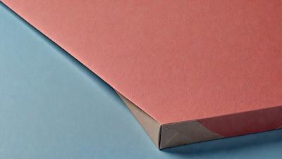 The primary subject of the image is a pink piece of paper. The setting is a blue surface, which could be a table or a wall. The visual style is a close-up of the pink paper, showcasing its texture and color. The colors and mood of the image are predominantly pink and blue, creating a calm and soothing atmosphere.