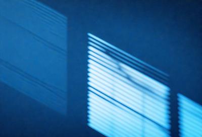 The primary subject of the image is a window with a view of the outside. The setting is a dark room, and the visual style appears to be a photo. The colors and mood of the image are predominantly dark, with a sense of mystery and intrigue.
