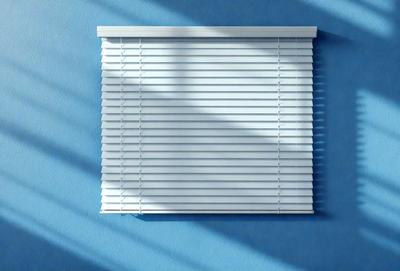 The primary subject of the image is a white shade, which is a part of a window blind. The shade is hanging on a blue wall, creating a contrast between the white shade and the blue background. The visual style of the image is a photo, capturing the details of the shade and the wall. The colors and mood of the image are predominantly blue, with the white shade adding a touch of brightness to the scene.