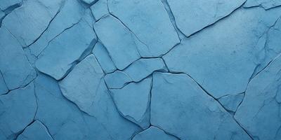The primary subject of the image is a blue stone wall with cracks and chips. The setting is a blue background, which adds to the visual style. The image is a photo, capturing the natural texture and appearance of the stone wall. The dominant colors are blue and grey, creating a calm and serene atmosphere.