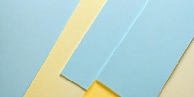 The primary subject of the image is a stack of three different colored papers, which are yellow, blue, and green. The setting is a table, and the visual style is a close-up of the papers. The colors and mood of the image are vibrant and lively, with the yellow, blue, and green papers creating a sense of freshness and energy.