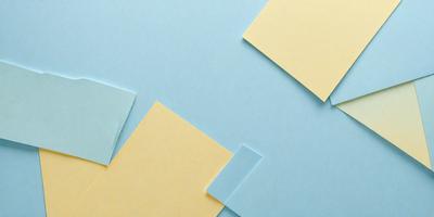 The primary subject of the image is a stack of yellow and blue sticky notes. The setting is a blue surface, which could be a table or a wall. The visual style is a close-up of the sticky notes, showcasing their colors and textures. The overall atmosphere is bright and cheerful, as the yellow and blue notes create a vibrant and lively scene.
