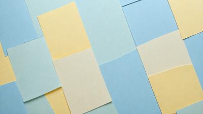 The primary subject of the image is a collection of yellow and blue post-it notes. The setting is a blue and yellow background, which creates a visually appealing contrast with the post-it notes. The visual style is a close-up of the post-it notes, showcasing their colors and textures. The overall atmosphere is bright and cheerful, with the blue and yellow colors evoking a sense of positivity and creativity.