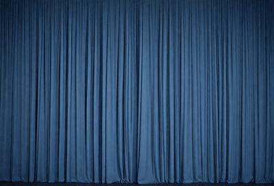 The primary subject of the image is a blue curtain. The setting is a stage or theater, with the curtains covering the stage. The visual style is a photo, and the dominant colors are blue and black. The overall atmosphere is dramatic and theatrical.