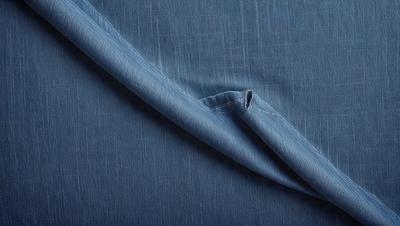 The primary subject of the image is a blue sheet with a hole in it. The setting is a bed, and the visual style is a photo. The colors and mood of the image are predominantly blue, giving it a calm and serene atmosphere.