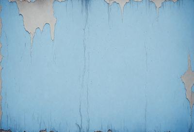 The primary subject of the image is a blue wall with a peeling paint texture. The setting is a room with a blue wall, and the visual style is a close-up of the wall. The dominant colors are blue and white, and the overall atmosphere is somewhat distressed or aged.