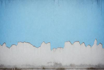 The primary subject of the image is a large, white wall with a blue sky in the background. The setting appears to be an outdoor environment, possibly a beach or a coastal area. The visual style of the image is a combination of photo and digital art, creating a unique and artistic representation of the scene. The dominant colors in the image are blue and white, with the blue sky providing a calming and serene atmosphere.