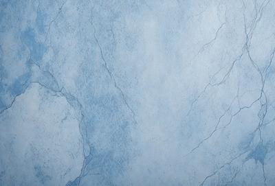 The primary subject of the image is a blue wall with a cracked and chipped appearance. The setting is a room with a blue-gray color scheme. The visual style is a close-up of the wall, showcasing its texture and imperfections. The colors and mood of the image are predominantly blue and gray, creating a calm and serene atmosphere.