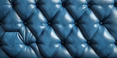 The primary subject of the image is a blue leather couch with a blue velvet cushion. The setting is a room with a blue background. The visual style is a close-up of the couch, showcasing its design and texture. The colors and mood of the image are predominantly blue, creating a calm and relaxing atmosphere.