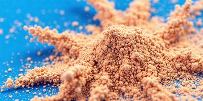 The primary subject of the image is a pile of brown powder, which appears to be a mix of sand and flour. The setting is a blue surface, possibly a table or a countertop. The visual style of the image is a close-up of the powder, showcasing its texture and color. The dominant colors in the image are brown and blue, creating a warm and inviting atmosphere.