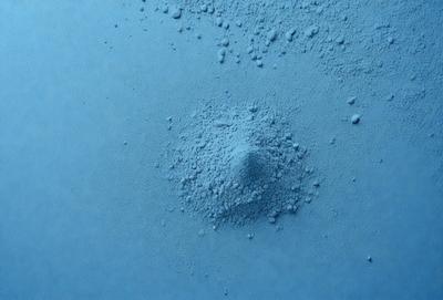 The primary subject of the image is a blue substance, possibly a powder or a liquid, with a small hole in the center. The setting is a blue surface, which could be a table or a wall. The visual style appears to be a close-up of the blue substance, possibly a photo or a digital artwork. The colors and mood of the image are predominantly blue, giving it a calm and serene atmosphere.