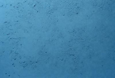 The primary subject of the image is a blue surface, which appears to be a wall or a piece of artwork. The setting is indoors, and the visual style is a close-up of the blue surface. The colors and mood of the image are predominantly blue, creating a calm and serene atmosphere.