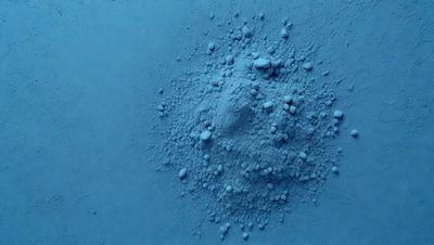The primary subject of the image is a blue substance, possibly a powder or a liquid, with a cloudy appearance. The setting is a blue background, which creates a contrast with the blue substance. The visual style appears to be a close-up of the blue substance, possibly a photo or a digital artwork. The colors and mood of the image are predominantly blue, giving it a calm and serene atmosphere.