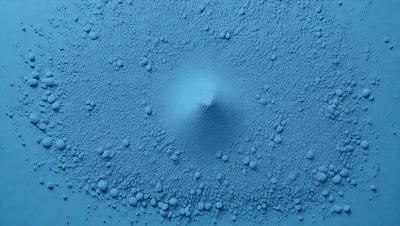 The primary subject of the image is a blue substance, possibly a liquid or a powder, with a central hole or bubble. The setting appears to be a blue background, which adds to the visual style. The colors and mood of the image are predominantly blue, creating a calm and serene atmosphere.