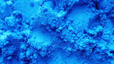 The primary subject of the image is a close-up of a blue substance, possibly a powder or a frothy liquid, with a blue background. The visual style appears to be a photo, as the image is in focus and the colors are vibrant. The dominant colors are blue and white, creating a calm and soothing atmosphere. The setting or background is a blue surface, which adds to the overall visual appeal of the image.