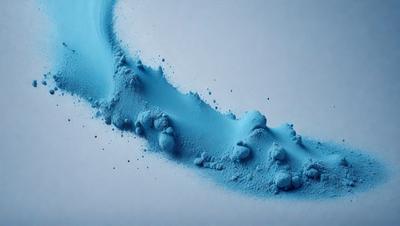 The primary subject of the image is a blue substance, possibly a powder or a liquid, that is being blown or dispersed. The setting is a white background, which provides a clean and uncluttered environment for the blue substance to be the main focus. The visual style of the image is a close-up, which emphasizes the details of the blue substance. The colors and mood of the image are predominantly blue, creating a sense of calmness and tranquility.
