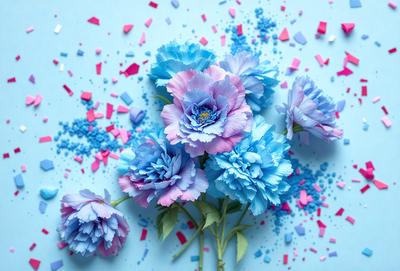 The primary subject of the image is a bouquet of colorful flowers, predominantly blue and pink, arranged in a vase. The flowers are placed on a blue surface, which adds a contrasting and vibrant touch to the scene. The visual style of the image is a combination of photo and digital art, creating a realistic yet artistic representation of the flowers. The colors and mood of the image are predominantly warm and cheerful, with the blue and pink flowers evoking a sense of happiness and