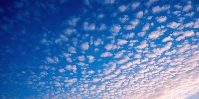 The primary subject of the image is a cloudy blue sky filled with fluffy white clouds. The setting is a vast, open sky, and the visual style is a natural, outdoor atmosphere. The colors and mood of the image are predominantly blue and white, creating a serene and peaceful ambiance.