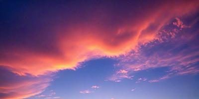 The primary subject of the image is a beautiful sunset with a pink sky. The setting is a cloudy sky, and the visual style is a photo. The colors and mood of the image are warm and serene, creating a peaceful atmosphere.