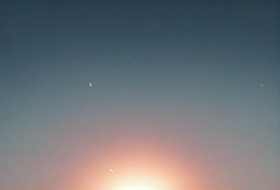 The primary subject of the image is the sun, which is rising in the sky. The setting is a clear blue sky, and the visual style is a photo. The colors and mood of the image are dominated by the warm hues of the sunrise, creating a serene and peaceful atmosphere.