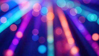 The primary subject of the image is a colorful, rainbow-like light display. The setting is a dark background, which contrasts with the vibrant colors of the light display. The visual style appears to be a combination of a photo and digital art, creating a unique and eye-catching effect. The dominant colors in the image are a mix of blue, green, and orange, creating a lively and energetic atmosphere.