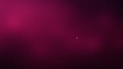The primary subject of the image is a moon, which is the main object in the scene. The setting is a dark, pinkish sky, which serves as the backdrop for the moon. The visual style of the image is a photo, capturing the moon in its natural environment. The colors and mood of the image are predominantly dark and moody, with the pinkish hue of the sky adding a sense of warmth and depth to the scene.