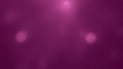 The primary subject of the image is a purple background with a few white dots. The setting appears to be a dark room, and the visual style is a close-up of the purple background. The colors and mood of the image are predominantly purple and dark, creating a moody atmosphere.