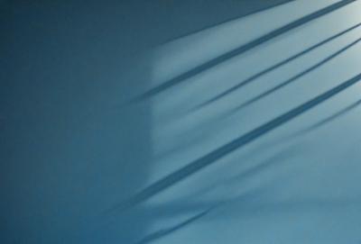 The primary subject of the image is a shadow of a window on a wall. The setting is a room with a blue wall, and the visual style appears to be a photo. The dominant colors are blue and white, creating a calm and serene atmosphere.
