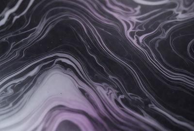 The primary subject of the image is a close-up of a marbled surface, which appears to be a black and purple pattern. The setting is a dark background, which contrasts with the marbled surface. The visual style is a close-up of the marbled surface, showcasing its intricate patterns. The colors and mood of the image are predominantly dark, with the marbled surface providing a sense of depth and complexity.