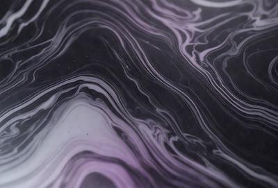The primary subject of the image is a close-up of a marbled surface, which appears to be a black and purple pattern. The setting is a dark background, which contrasts with the marbled surface. The visual style is a close-up of the marbled surface, showcasing its intricate patterns. The colors and mood of the image are predominantly dark, with the marbled surface providing a sense of depth and complexity.
