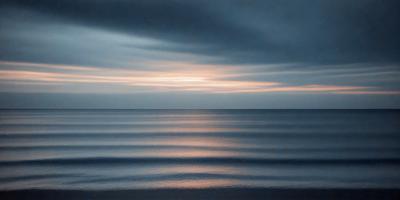 The primary subject of the image is the ocean, with a beautiful sunset in the background. The setting is a vast expanse of water, and the visual style is a photo of the ocean at sunset. The colors and mood of the image are serene and calming, with the warm hues of the sunset creating a peaceful atmosphere.