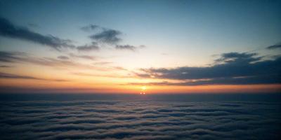 The primary subject of the image is the sunset, with the sun setting behind a cloudy sky. The setting is a cloudy sky, and the visual style is a photo. The colors and mood of the image are dominated by the warm hues of the sunset and the cloudy sky, creating a serene and peaceful atmosphere.