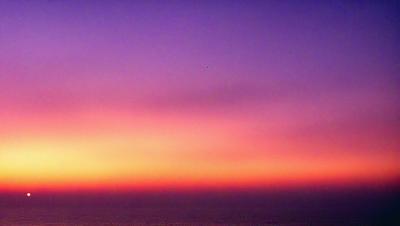 The primary subject of the image is a beautiful sunset, with the sky filled with warm hues and a purple tint. The setting is a vast ocean, with the sun's rays reflecting off the water, creating a serene and picturesque scene. The visual style of the image is a photo, capturing the stunning colors and the vast expanse of the ocean. The colors and mood of the image are calming and peaceful, evoking a sense of tranquility and awe at the beauty