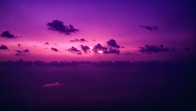 The primary subject of the image is a beautiful sunset, with the sun peeking through the clouds. The setting is a cloudy sky, and the visual style is a photo. The dominant colors are purple and orange, creating a warm and serene atmosphere.