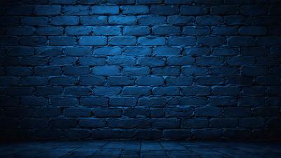 The primary subject of the image is a blue brick wall. The setting is a dark room with a blue brick wall as the main focus. The visual style is a photo, and the dominant colors are blue and black. The overall atmosphere is moody and dramatic.