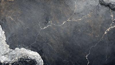 The primary subject of the image is a close-up of a black and white marble wall. The setting is a stone wall with a cracked pattern, giving it a textured and aged appearance. The visual style is a photo, capturing the intricate details of the marble surface. The colors and mood of the image are predominantly black and white, creating a sense of timelessness and elegance.
