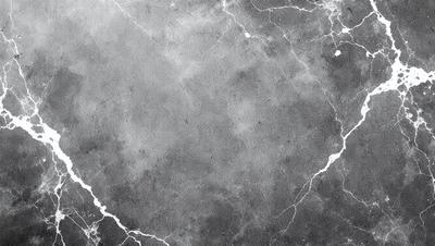 The primary subject of the image is a large, gray, marble-like surface. The setting is a dark, cloudy sky, which creates a moody atmosphere. The visual style is a black and white photo, giving the image a classic and timeless appearance. The colors and mood are predominantly dark and dramatic, with the gray marble surface contrasting against the cloudy sky.
